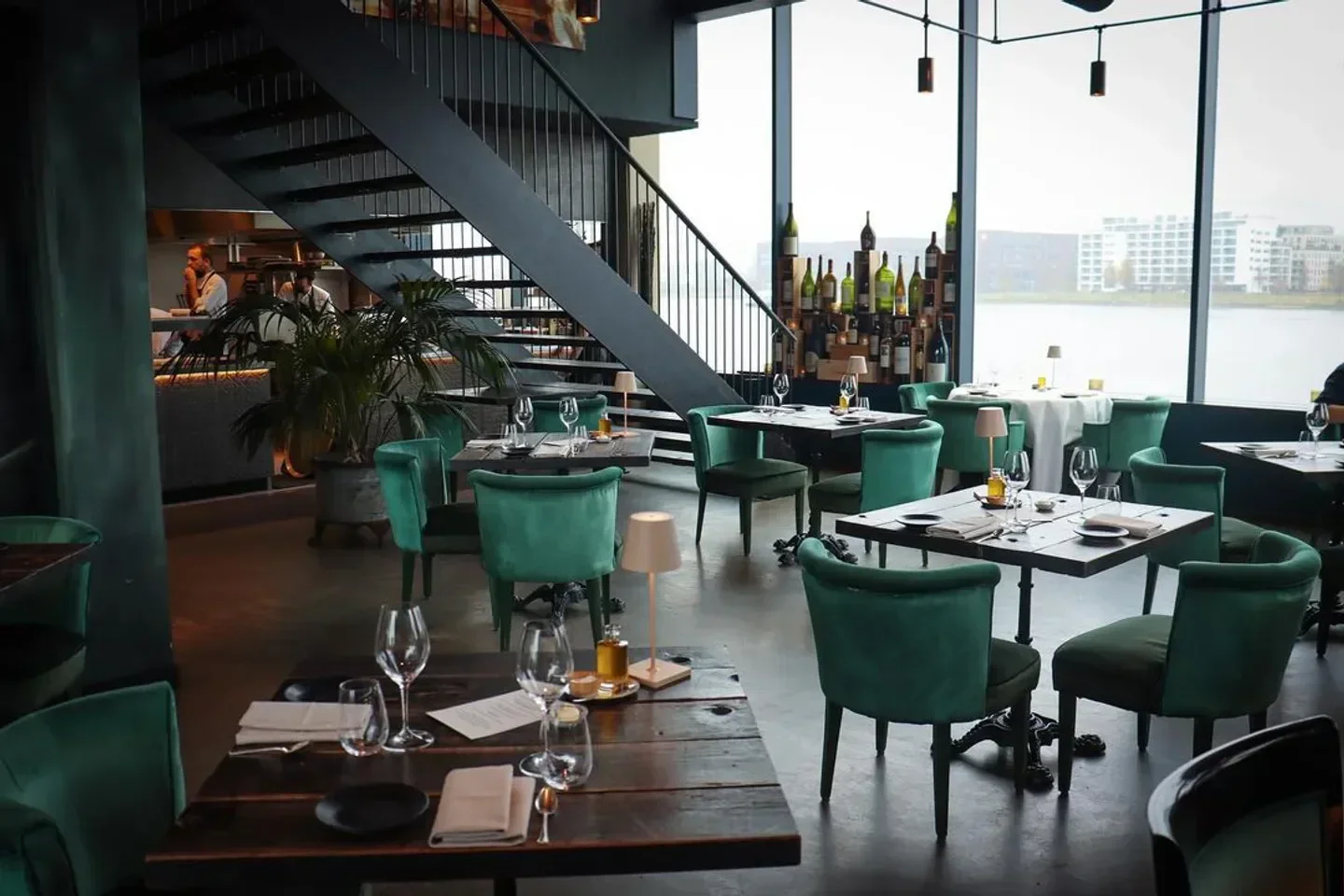Interior of MOS Amsterdam restaurant with green chairs and a view of the water.