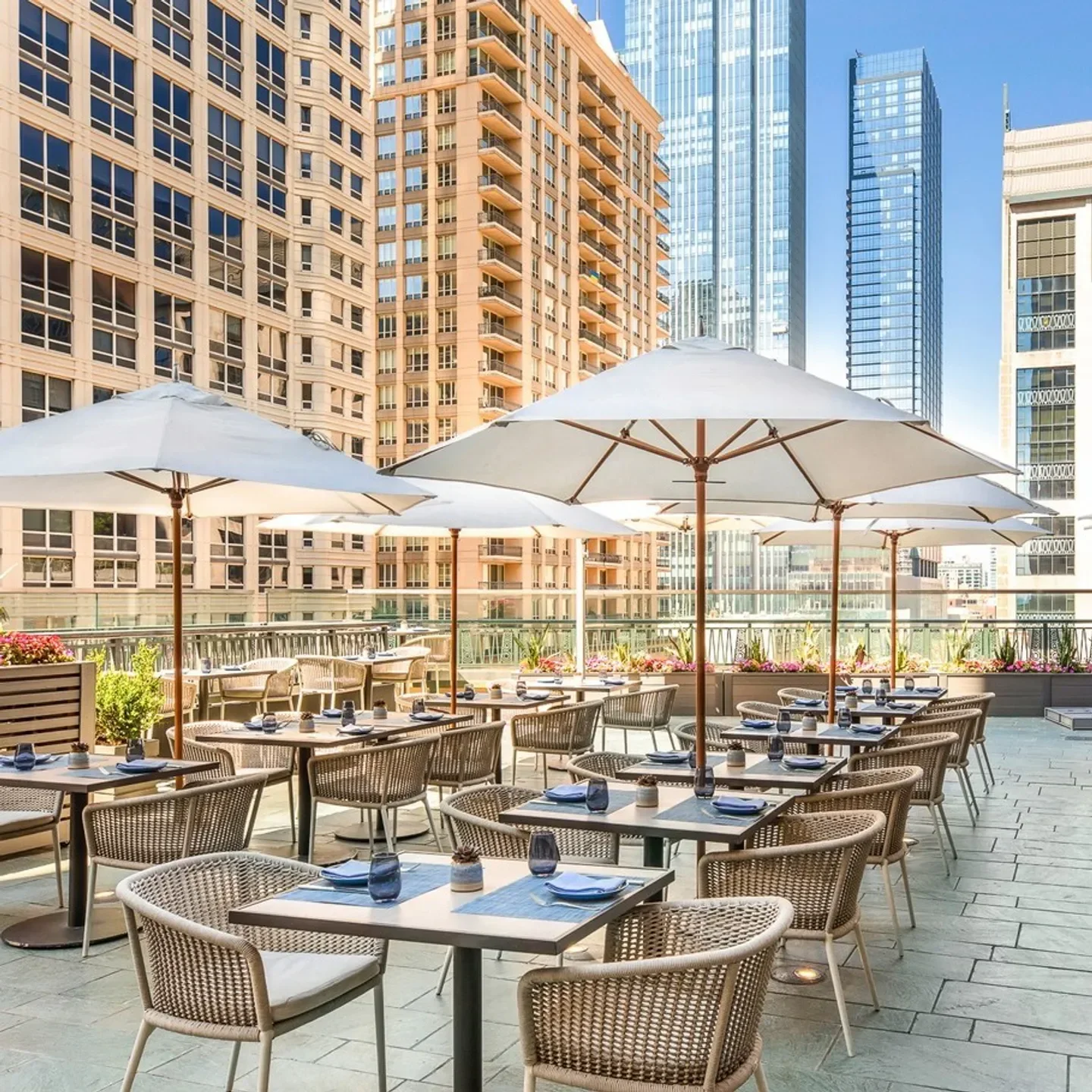 Outdoor dining at NoMI Kitchen in Chicago, featuring tables, umbrellas, and city views.