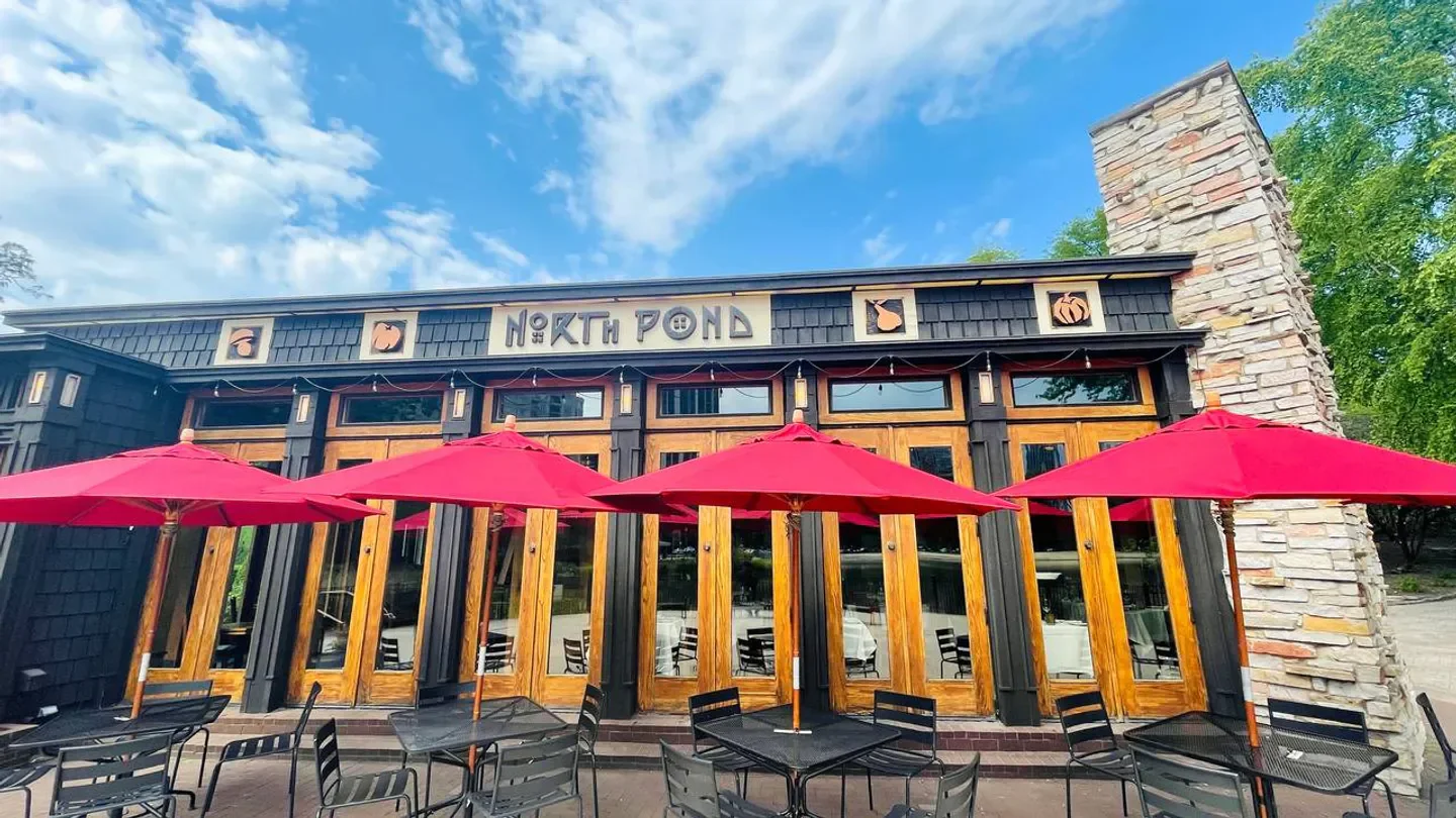 Exterior of North Pond restaurant in Chicago with red umbrellas and outdoor seating.
