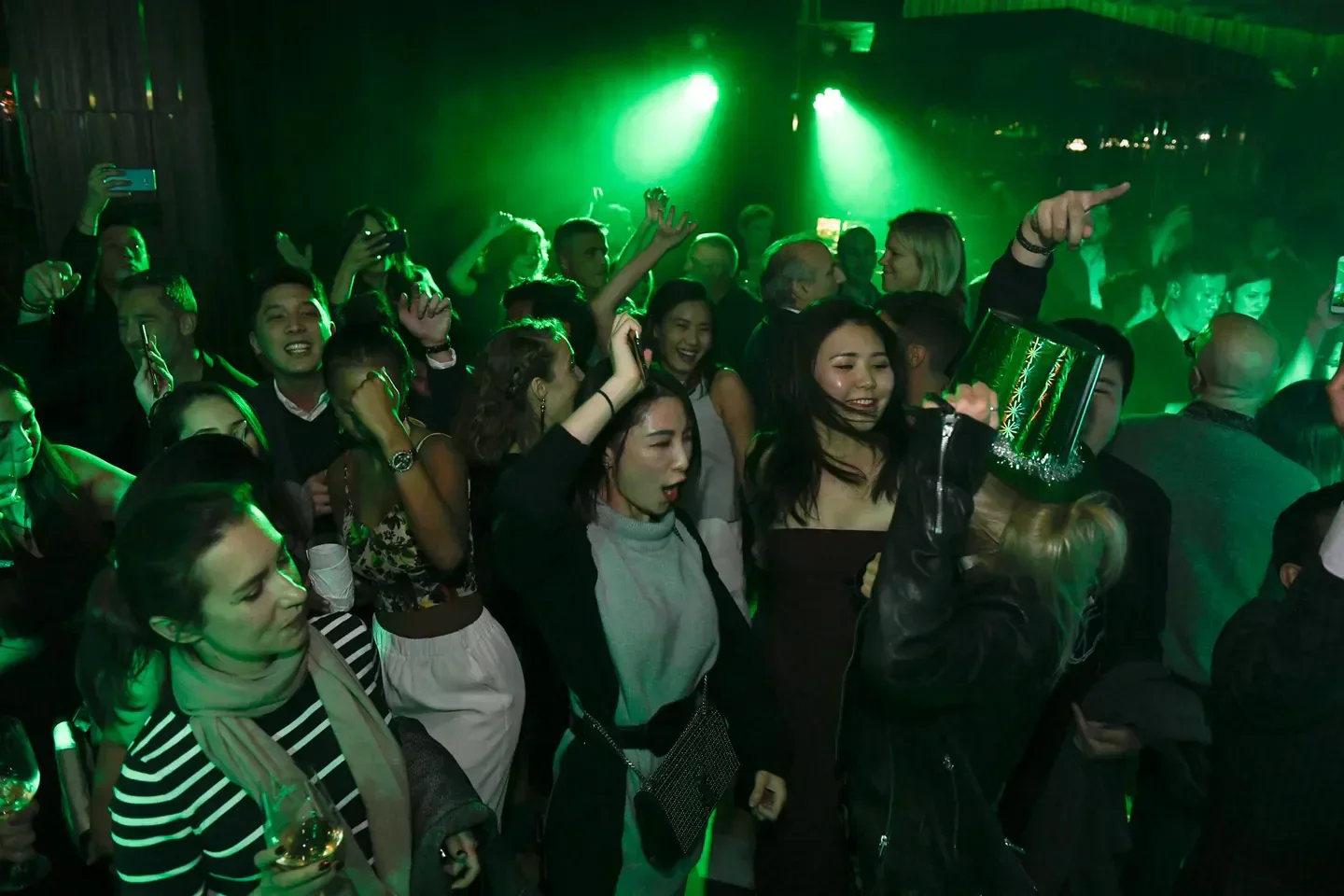 Energetic crowd partying at Ozone nightclub in Hong Kong, lit by green lights.