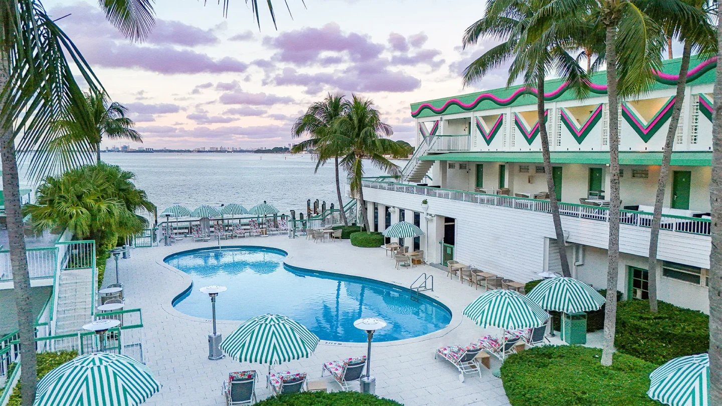 Palm Tree Club Miami features a kidney-shaped pool, striped umbrellas, and waterfront views.