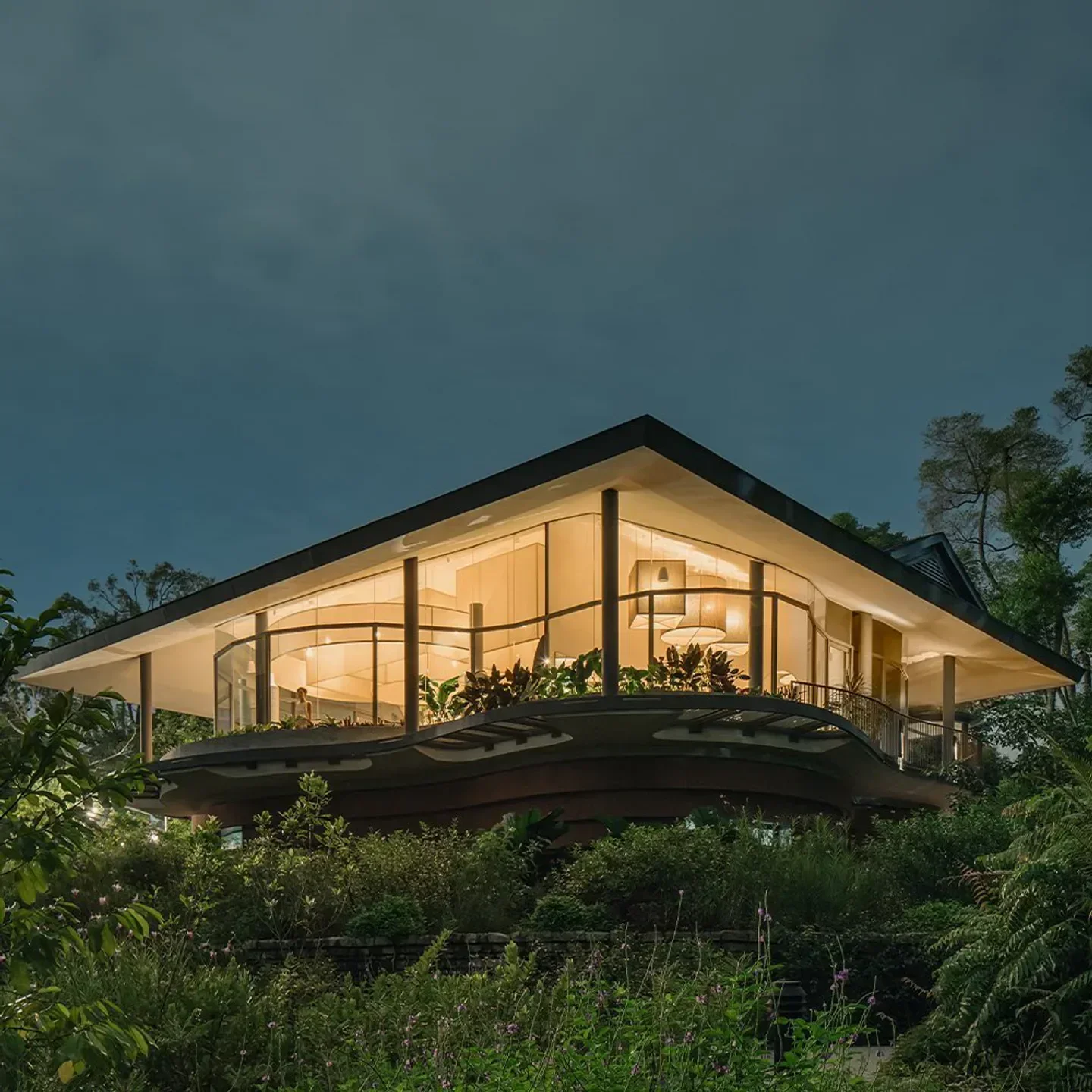 Pangium restaurant in Singapore, a modern building surrounded by lush greenery at dusk.