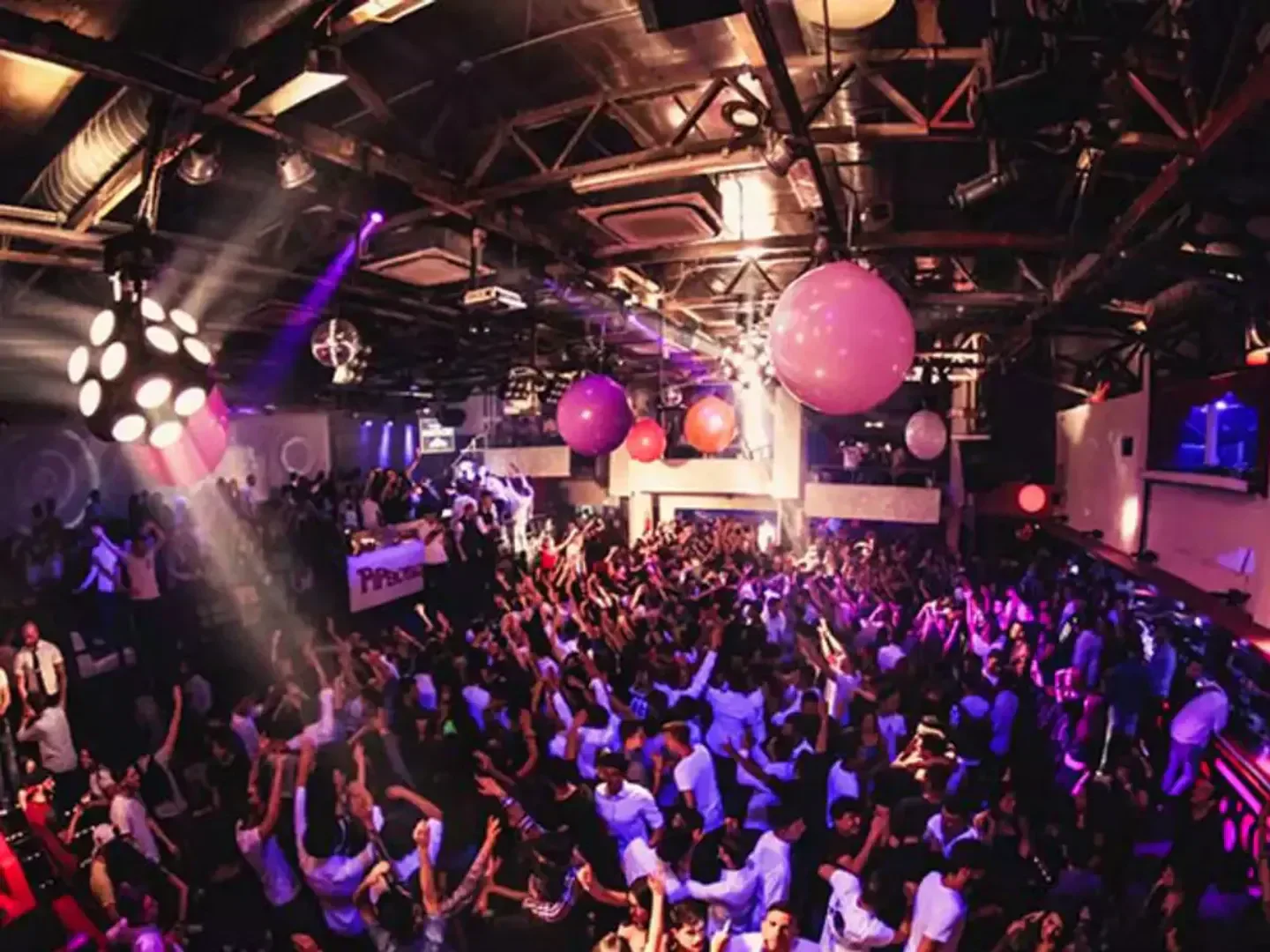 Energetic crowd partying at Piper Club in Rome, with colorful lights and balloons.