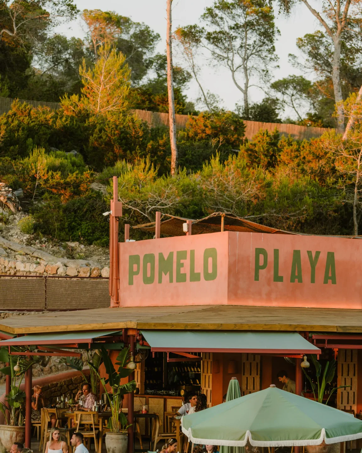 Pomelo Playa restaurant exterior with a lush hillside backdrop and outdoor seating in the city.
