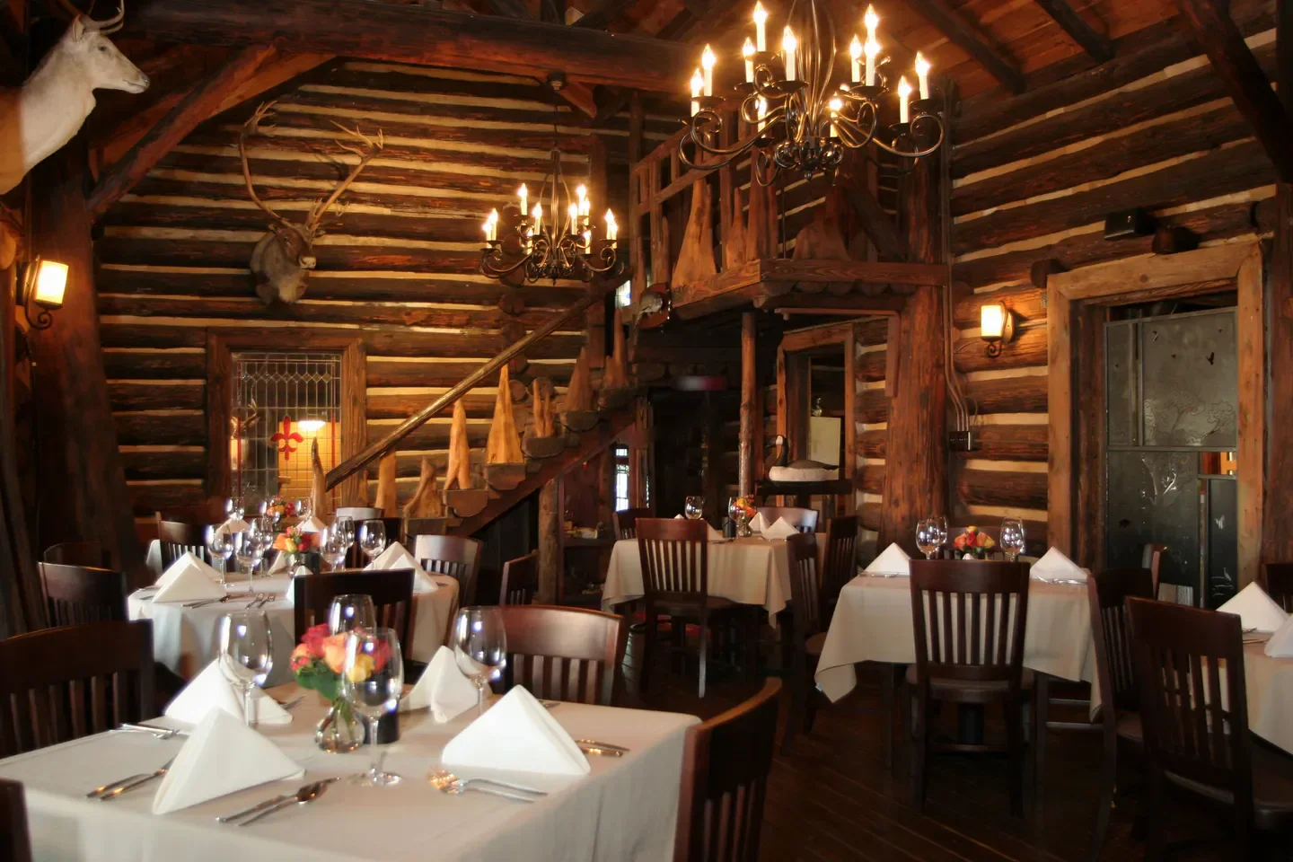 Cozy dining room at Rainbow Lodge in Houston with log walls and chandeliers.