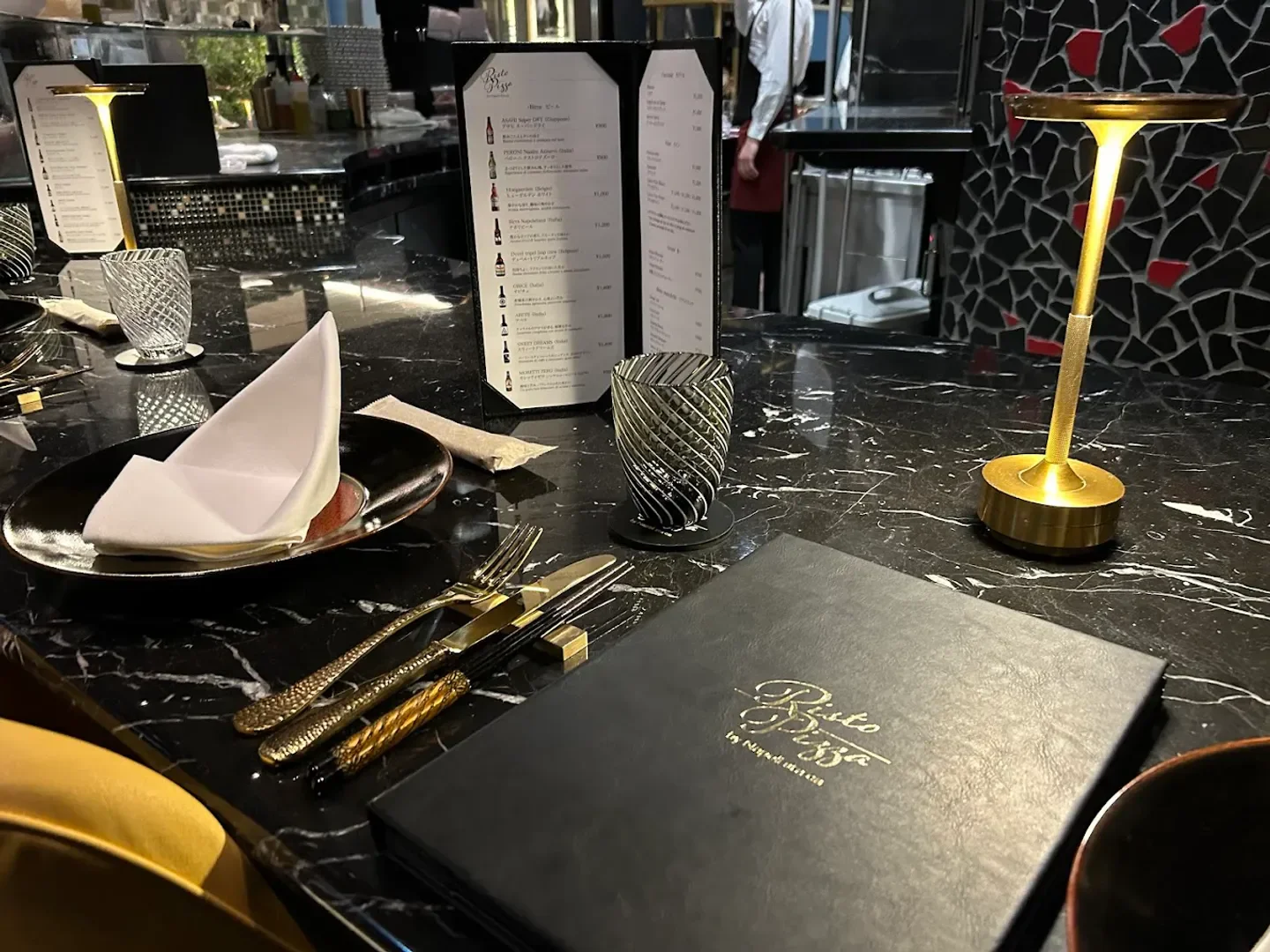Table setting with menu at RistoPizza in Tokyo, featuring stylish cutlery and lighting.