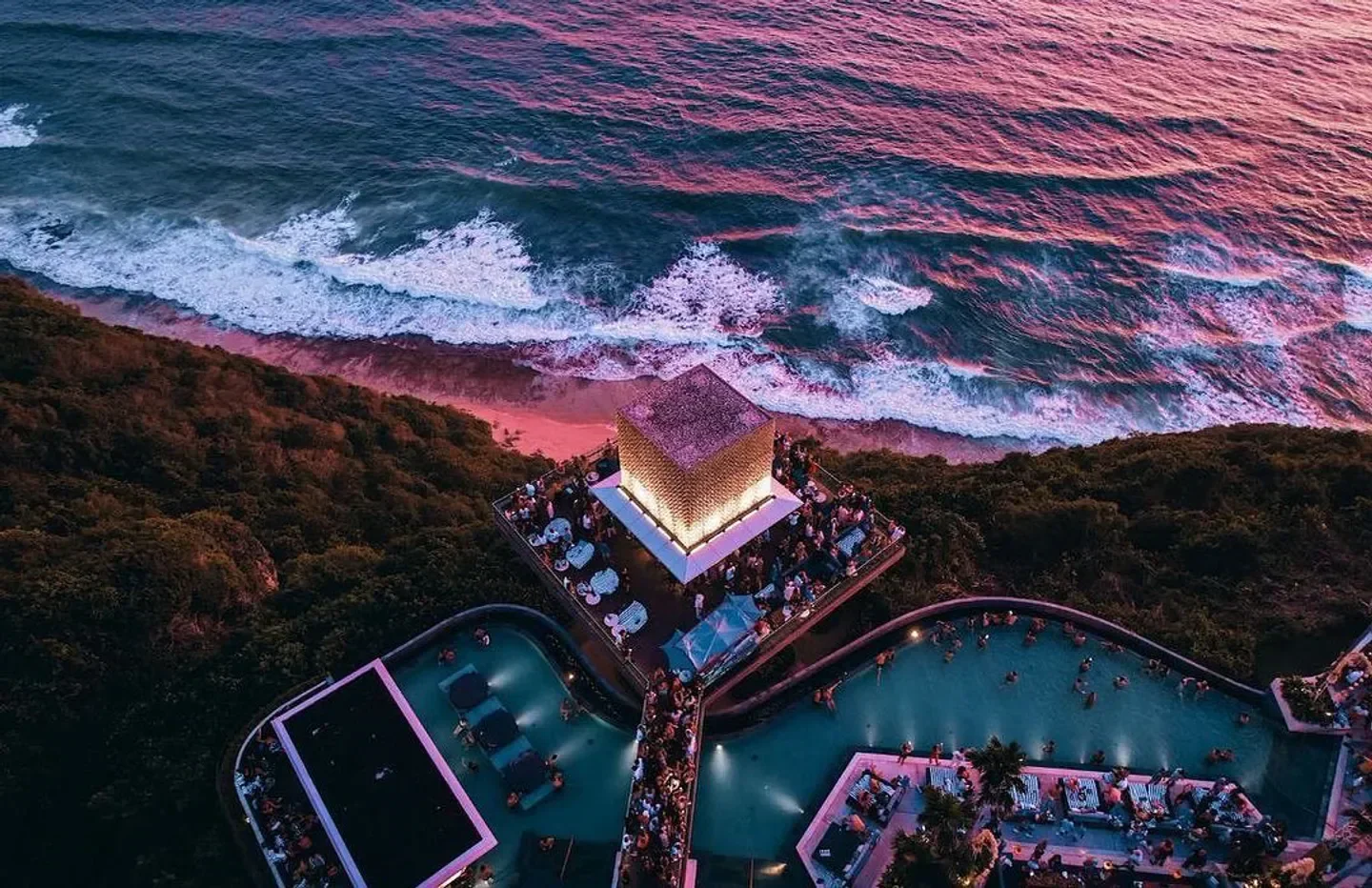 Aerial view of Savaya Bali beach club and pools in Bali, with ocean waves.