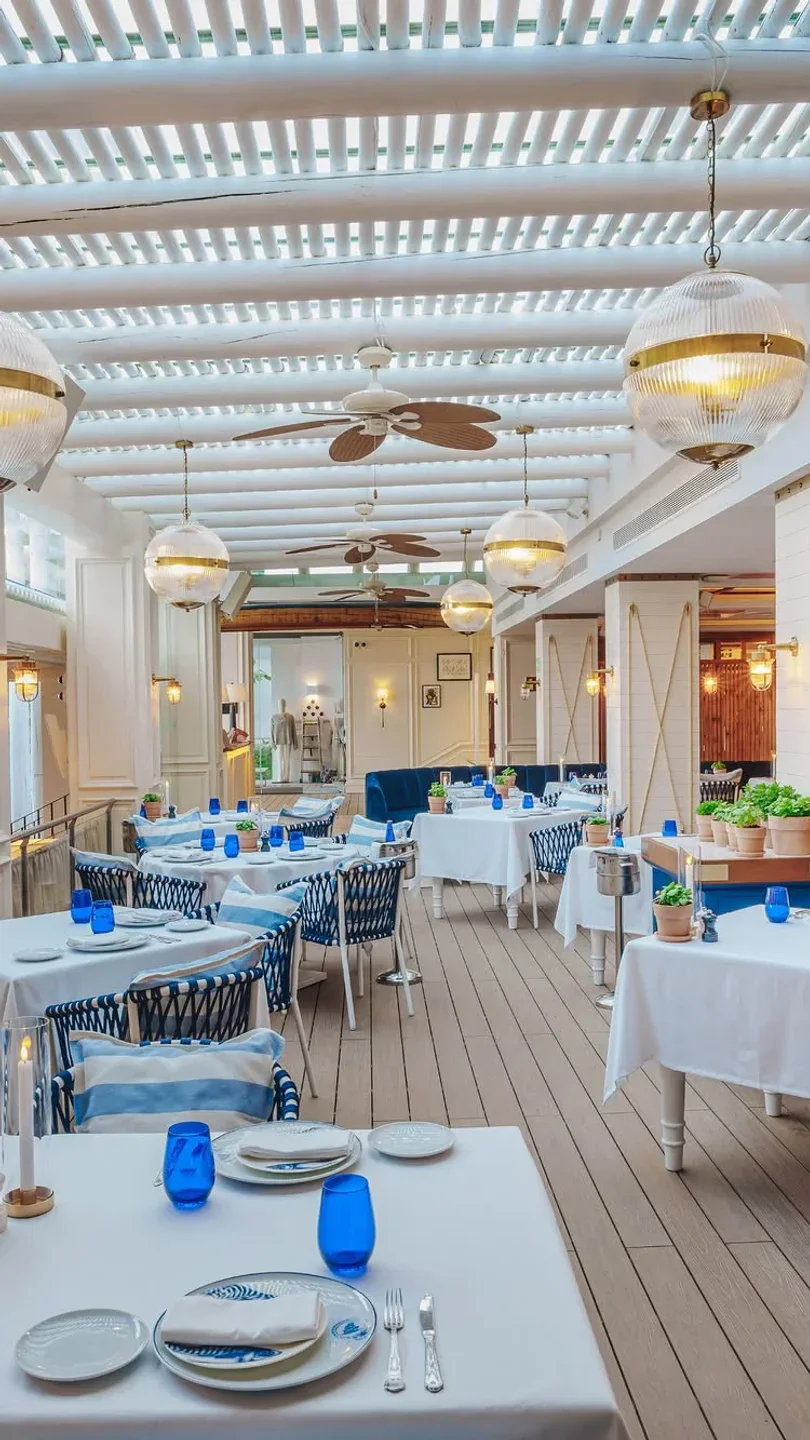 Elegant interior of Sea Grill restaurant in Marbella with white tables, blue accents, and stylish globe pendant lights.