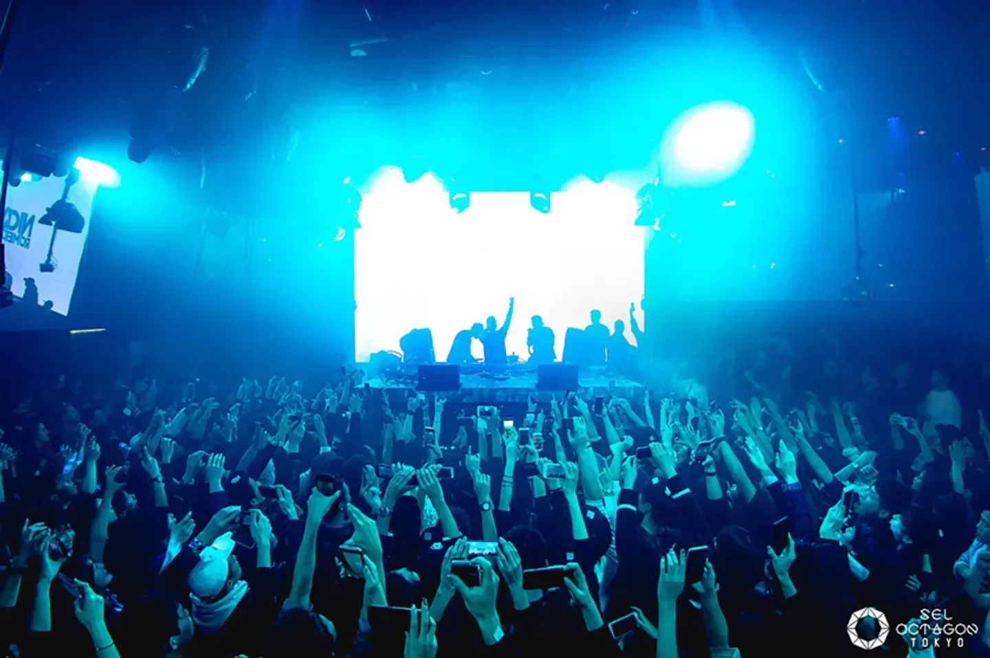 Energetic crowd at SEL Octagon nightclub in Tokyo, phones held up in the air.