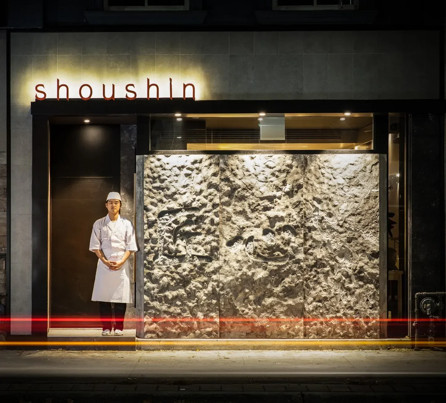 Chef outside Shoushin restaurant in Toronto, with textured stone wall and sign.