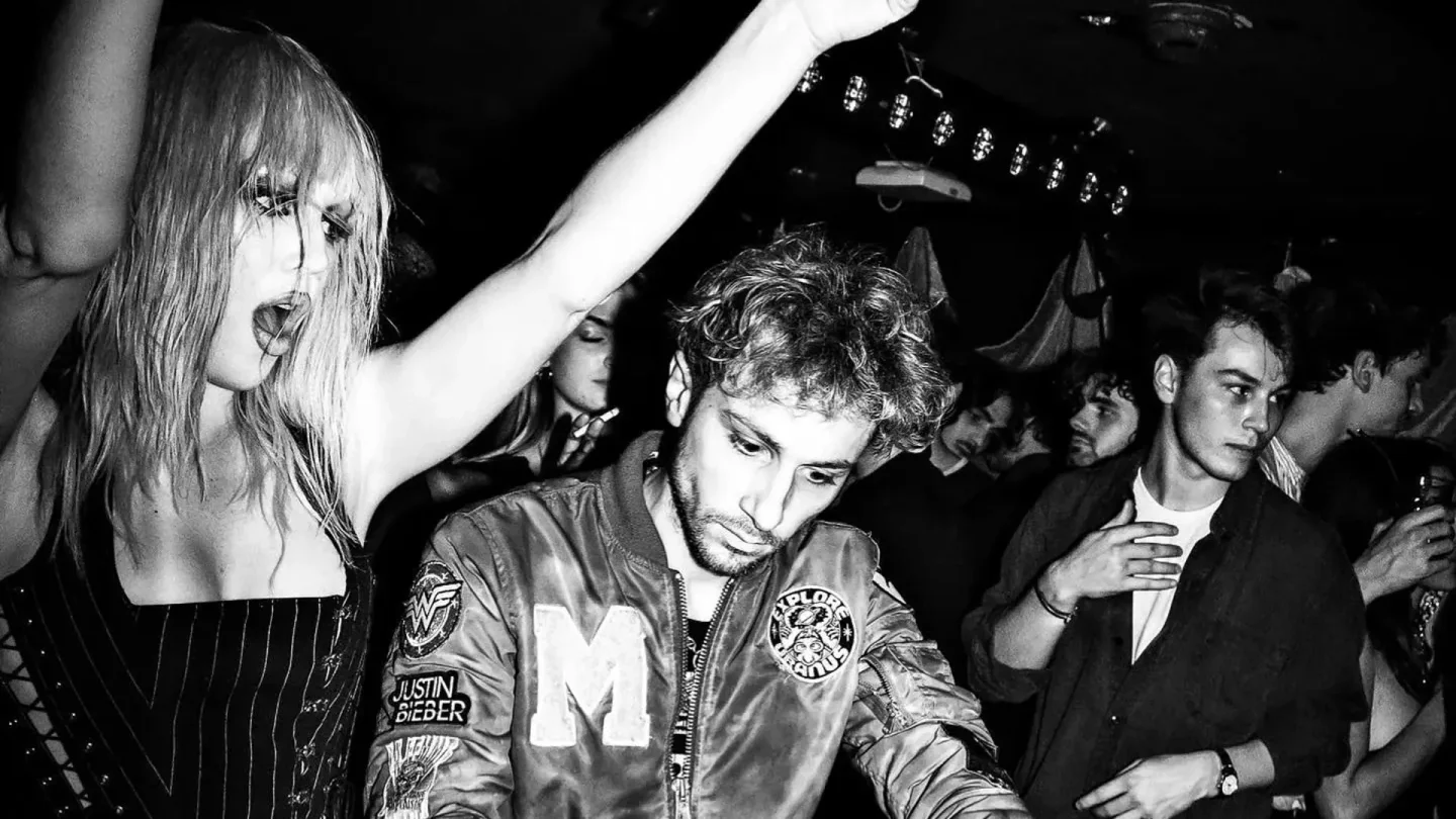 Energetic black and white photo of people dancing at Silencio Paris, featuring a woman joyfully raising her hand and a man in a decorated jacket moving to the rhythm.
