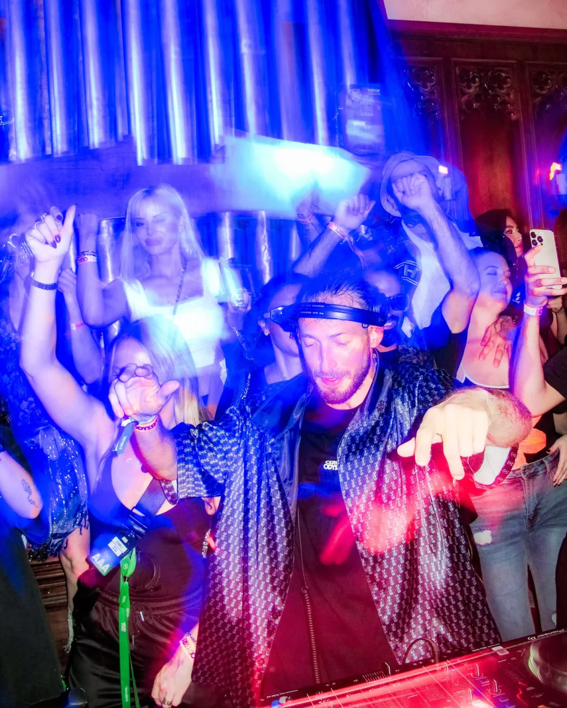 DJ performing for a crowd at Sinners y Santos nightclub, with blue and red lights illuminating the dance floor.