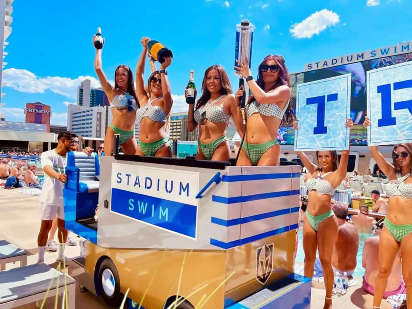 Stadium Swim in Las Vegas, women holding bottles of champagne and signs by the pool