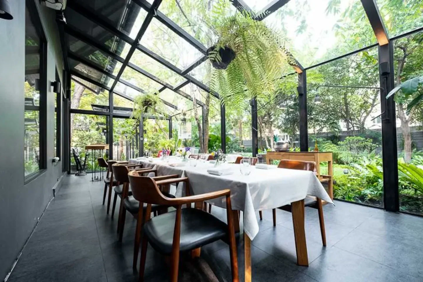 Dining space at Sühring restaurant in Bangkok, surrounded by lush greenery and natural light.