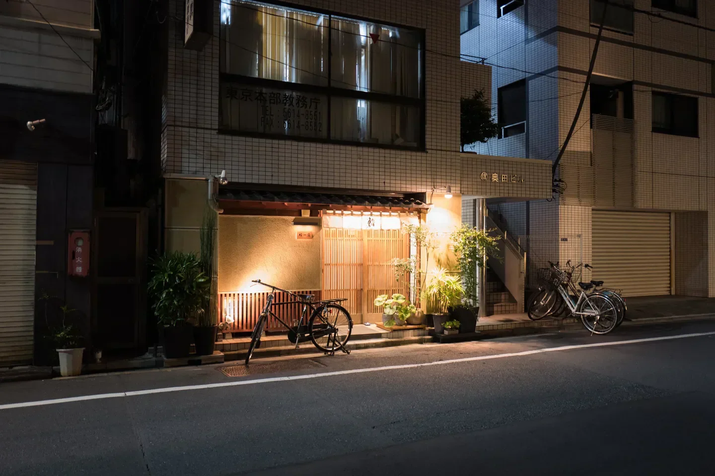 Exterior of Sushi Ichijo in Tokyo at night, featuring bicycles and illuminated entrance.