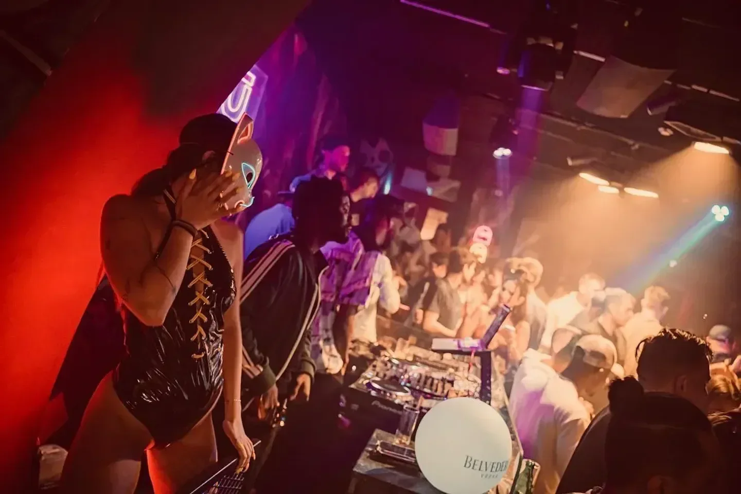 TABU Mykonos nightclub scene with DJ, masked dancer, and vibrant party atmosphere.