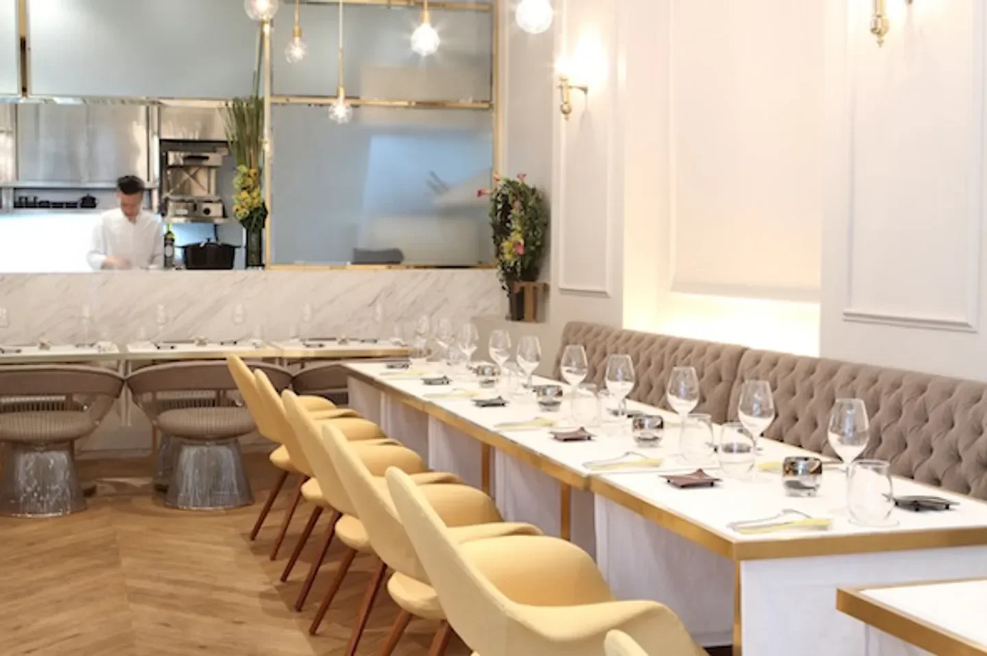 Elegant dining room interior at Tate restaurant in Hong Kong, with chef in the background.
