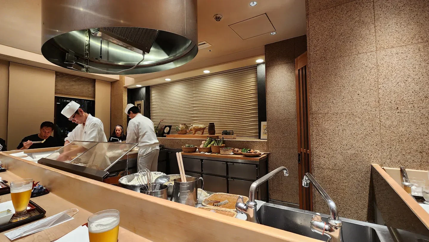 Chefs preparing food at Tempura Kondo, a Tokyo restaurant, with patrons and bar.