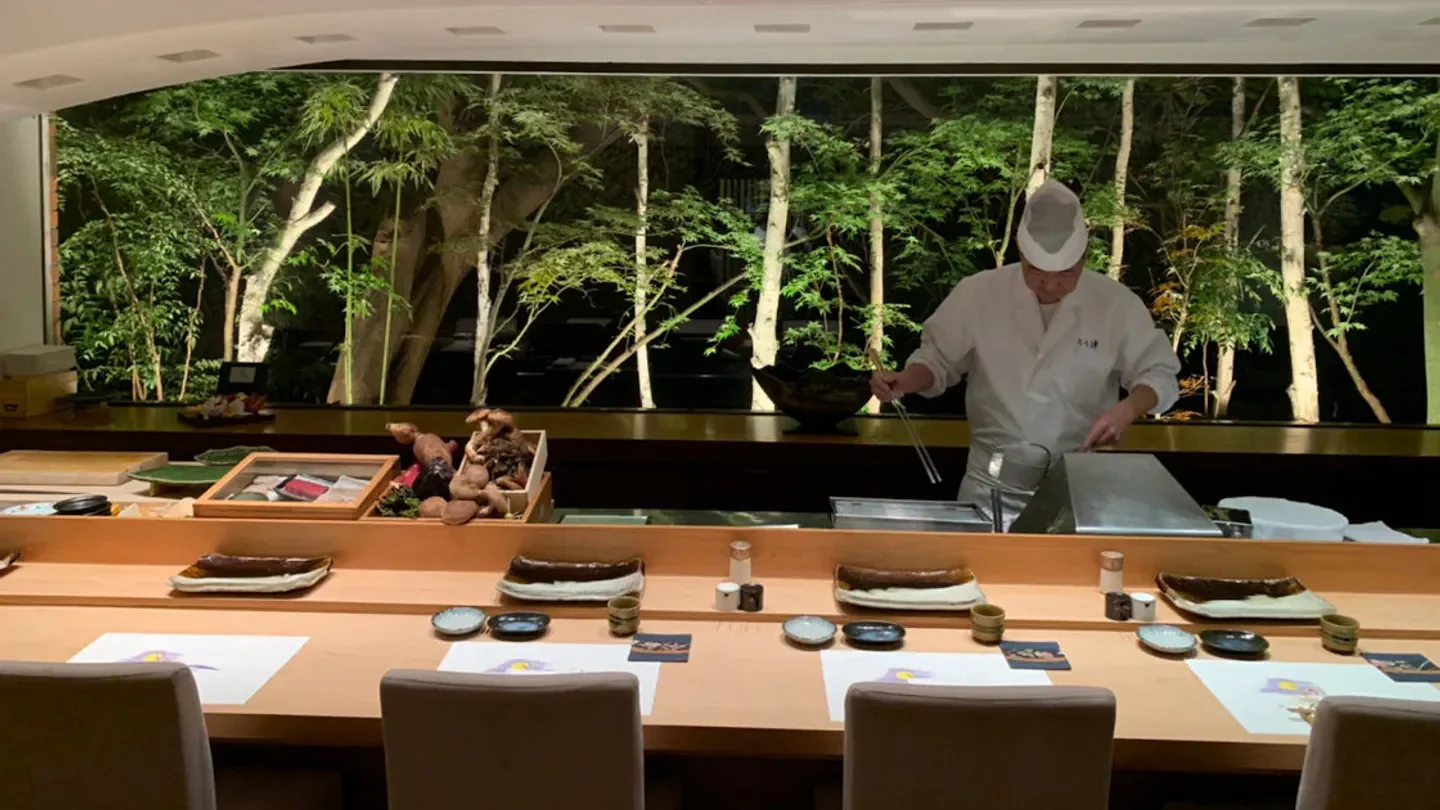 Chef preparing a dish at Tempura Uchitsu Hong Kong, with scenic outdoor views in the background.