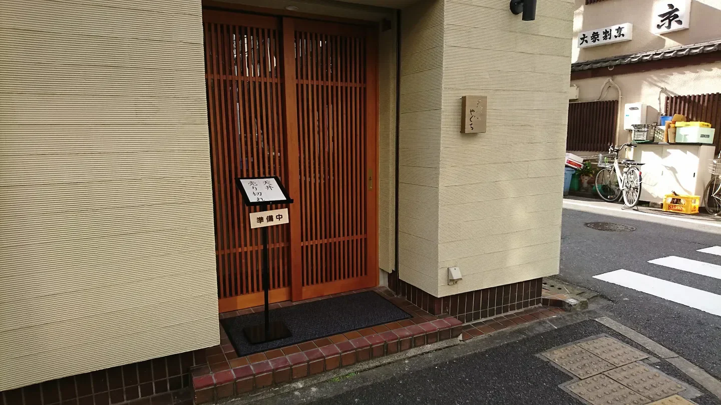 Entrance of Tempura Yaguchi in Tokyo, Japan, featuring wooden door and sign.
