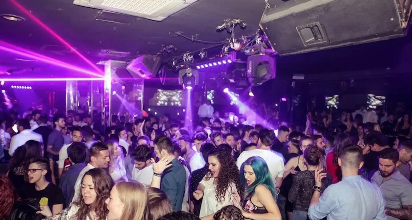 Energetic crowd partying at The Club in Milan, illuminated by purple laser lights.