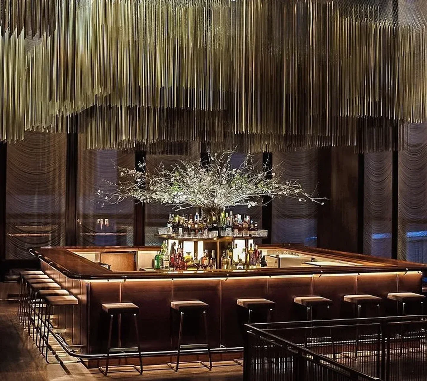 The Grill New York bar interior with luxurious wooden counter, plush stools, and dramatic overhead lighting.