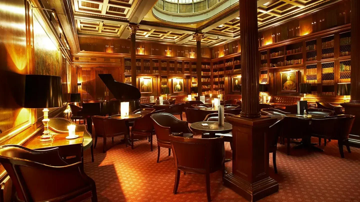 Interior view of The Library Bar in Copenhagen, featuring a grand piano and bookshelves.