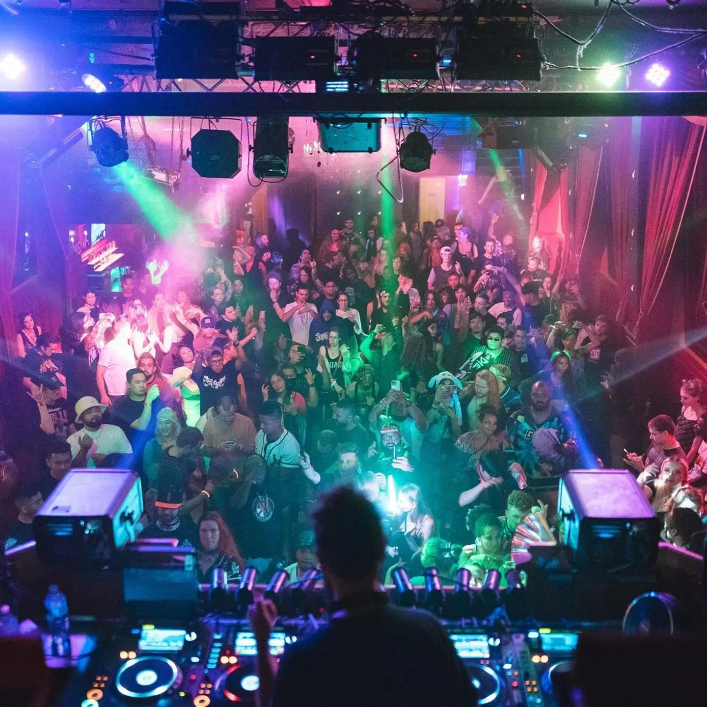 Energetic crowd at Trinity nightclub in Seattle, with DJ in the foreground and lights.