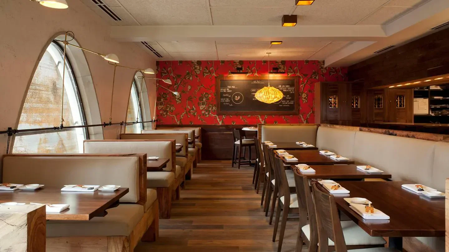 Interior dining space at Uchi Houston restaurant with wood tables and red floral wallpaper.