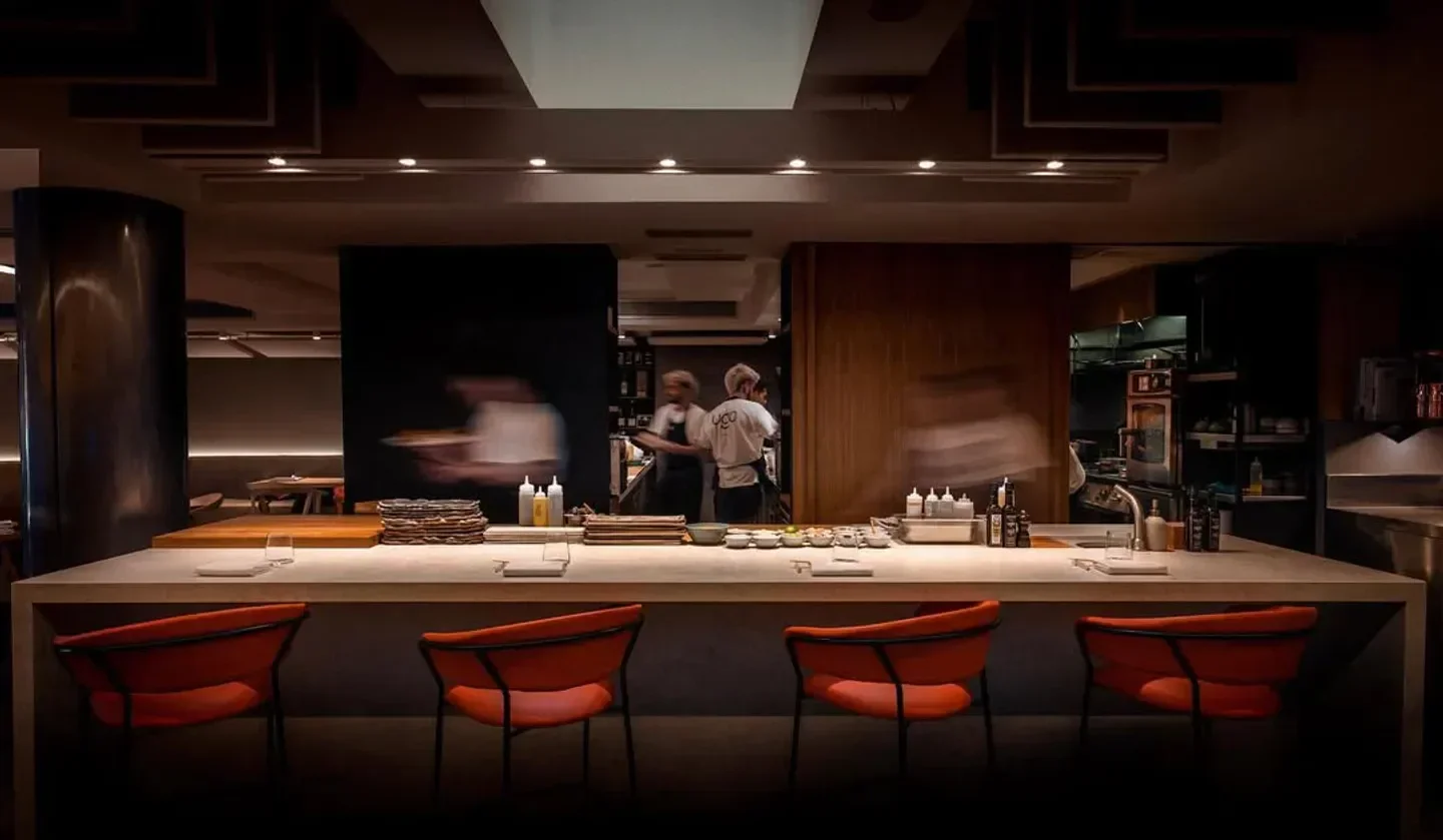 Interior of Ugo Chan restaurant in Madrid with bar seating and kitchen staff.