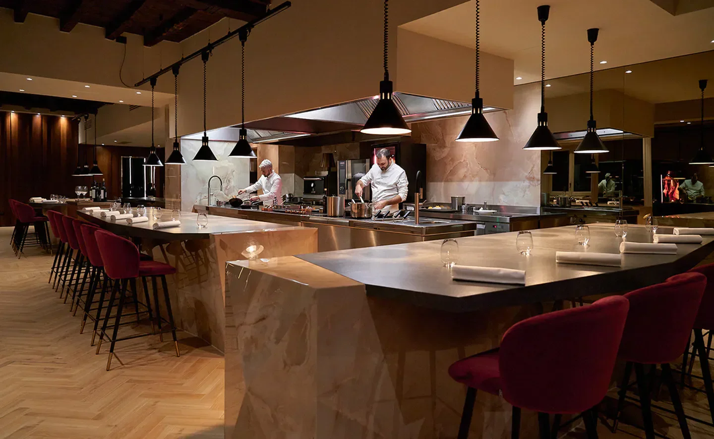 Chefs preparing food at Verso Capitaneo restaurant in Milan with stylish interior and bar seating.