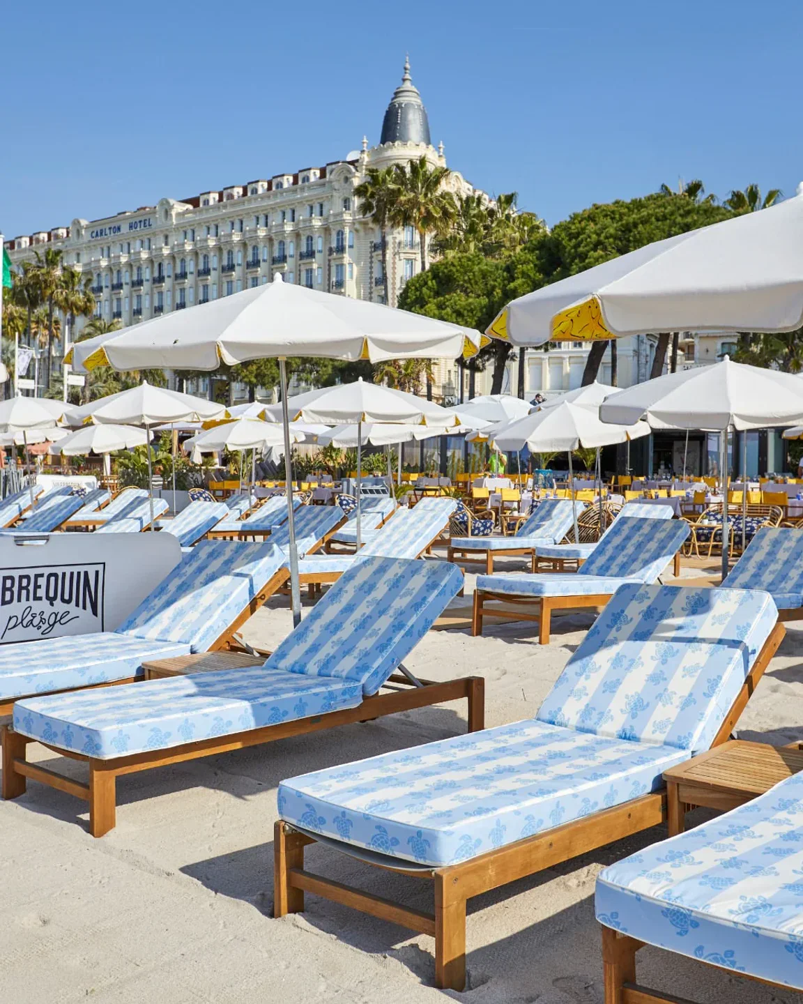 Vilebrequin La Plage beach club in Cannes with blue striped loungers and white umbrellas before Carlton Hotel.