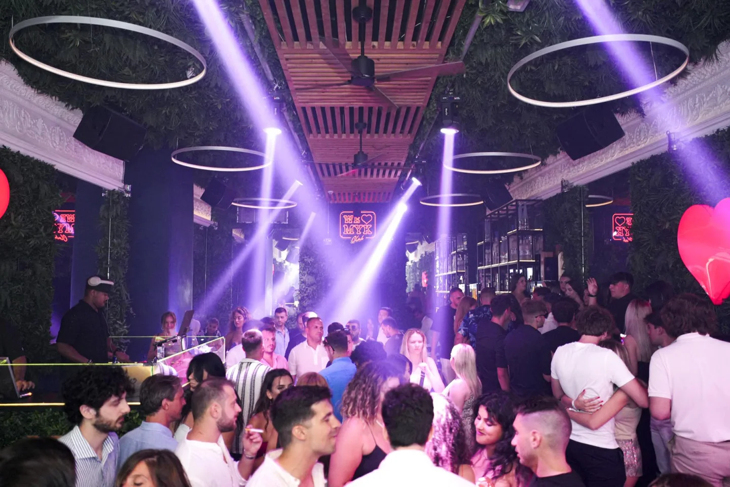 Lively interior of WE LOVE MYK nightclub in Mykonos with purple lights and lush greenery