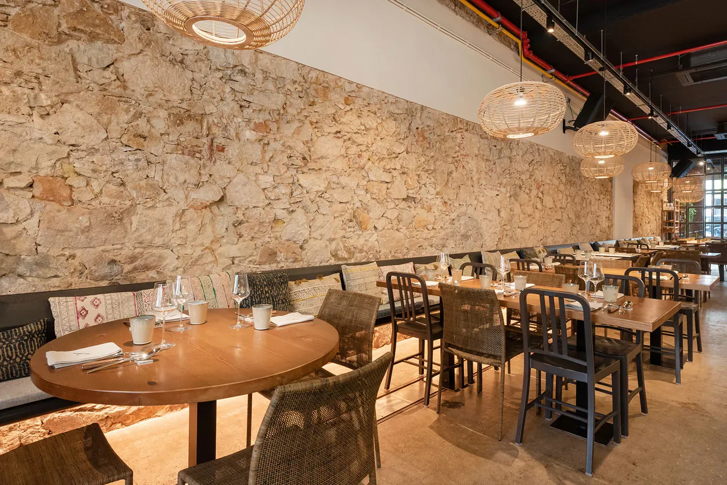 Interior of Xavier Pellicer in Barcelona, featuring rustic stone wall and woven lamps.
