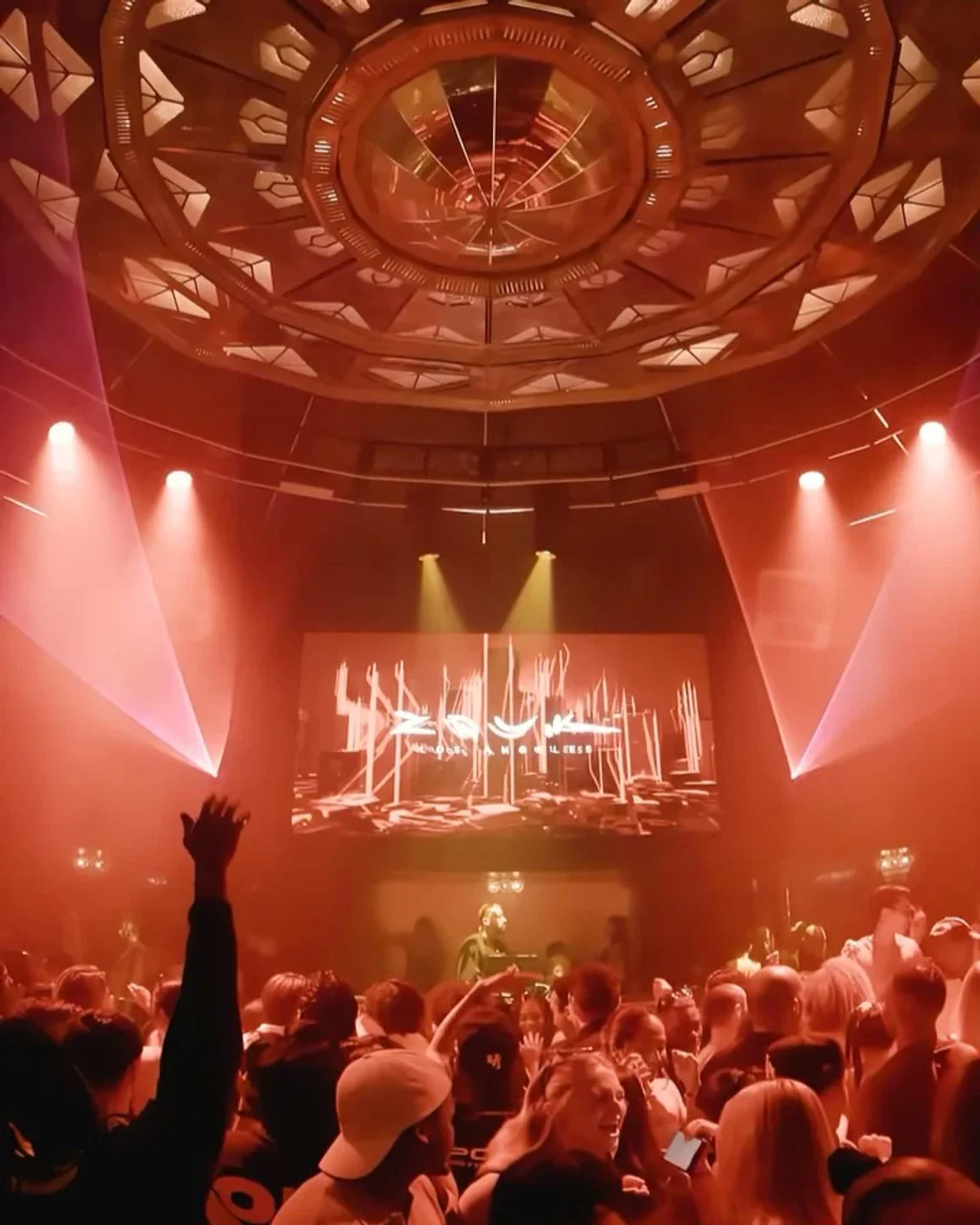 Energetic crowd enjoying a night at Zouk LA nightclub with vibrant laser lights and a large screen displaying the Zouk logo.