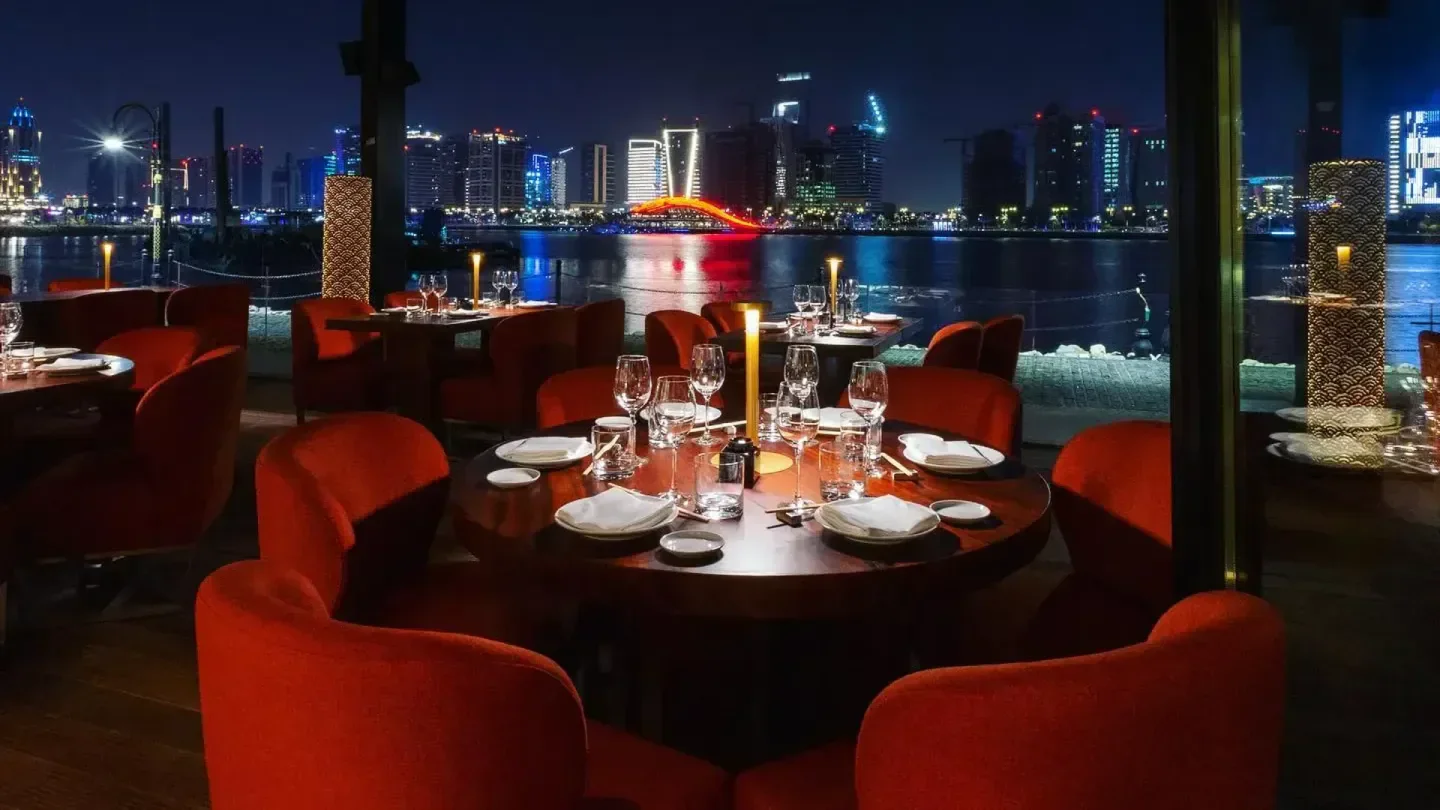 Zuma Doha: Night view of restaurant interior with city skyline and waterfront.